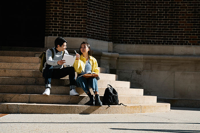 Woman and man meeting up on steps, discussing and sharing a tablet, representing co-parenting and secret child conversation.