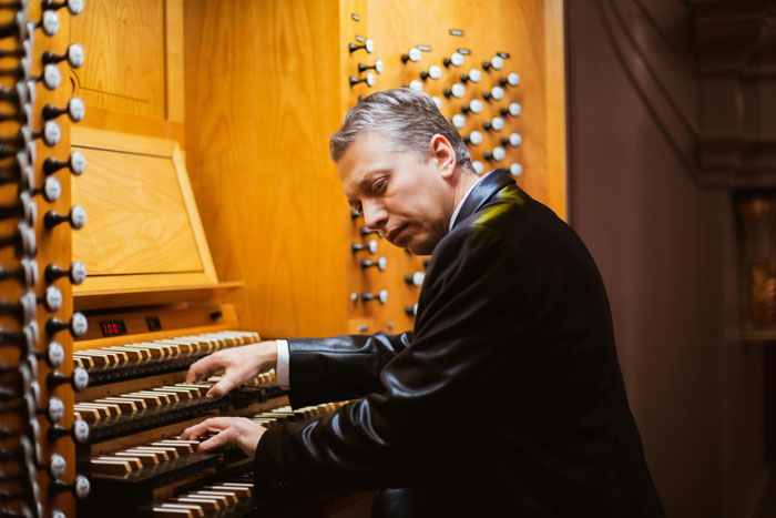 Man in black suit playing organ keys, illustrating guy agrees to perform at friends wedding but sues after no pay or invite