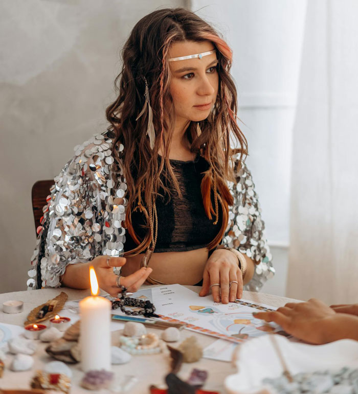 Woman with braided hair and silver shawl performing a ritual at a table, relating to sister’s rebirth party decision.